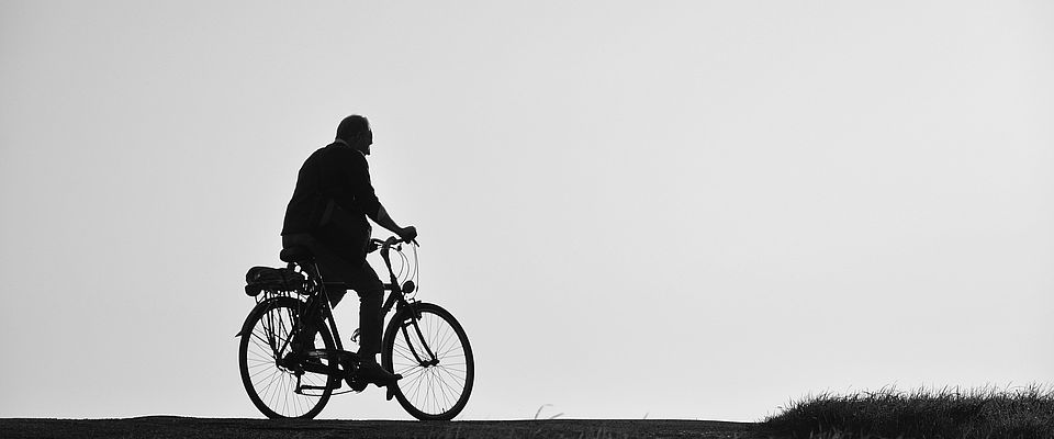 Älterer Herr auf einem Fahrrad fährt durch eine Landschaft